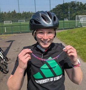 A student in a cycling helmet smiling and holding a bead necklace