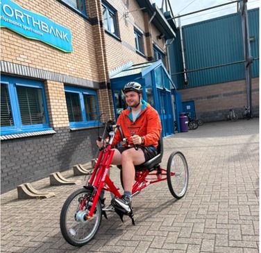A person riding a red hand cycle outside a sports centre