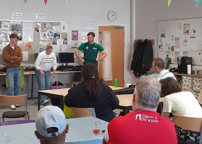 Students speaking to a seated group in a community room