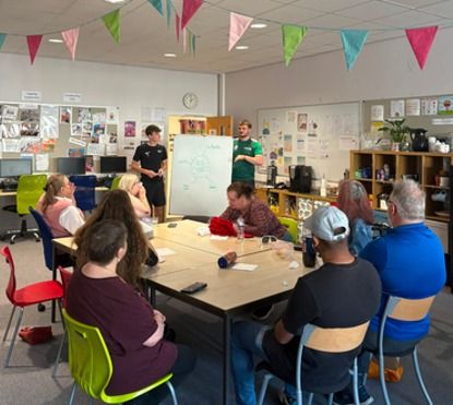 Students leading a discussion with a seated group, with a whiteboard behind them