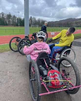 People using hand cycles beside a running track