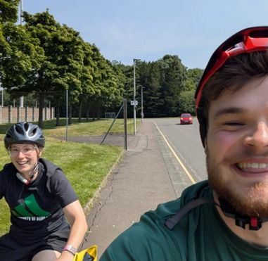 Two people in cycling helmets on a path, one riding an adaptive trike