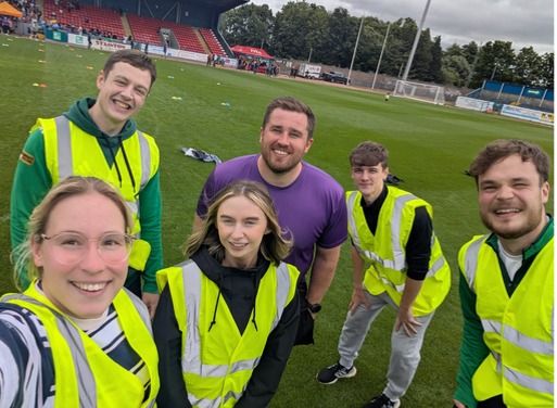 Students and colleagues in high-visibility jackets smiling on a sports pitch